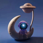 Cute astronaut toy sitting on crescent moon with UFO lamp, space-themed night light decor.