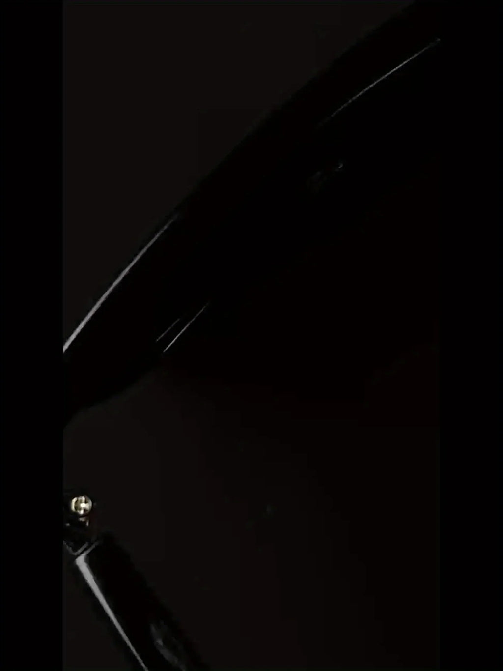 Close-up of glossy black electronic device with visible screw and curved edge on dark background