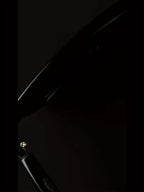 Close-up of glossy black electronic device with visible screw and curved edge on dark background