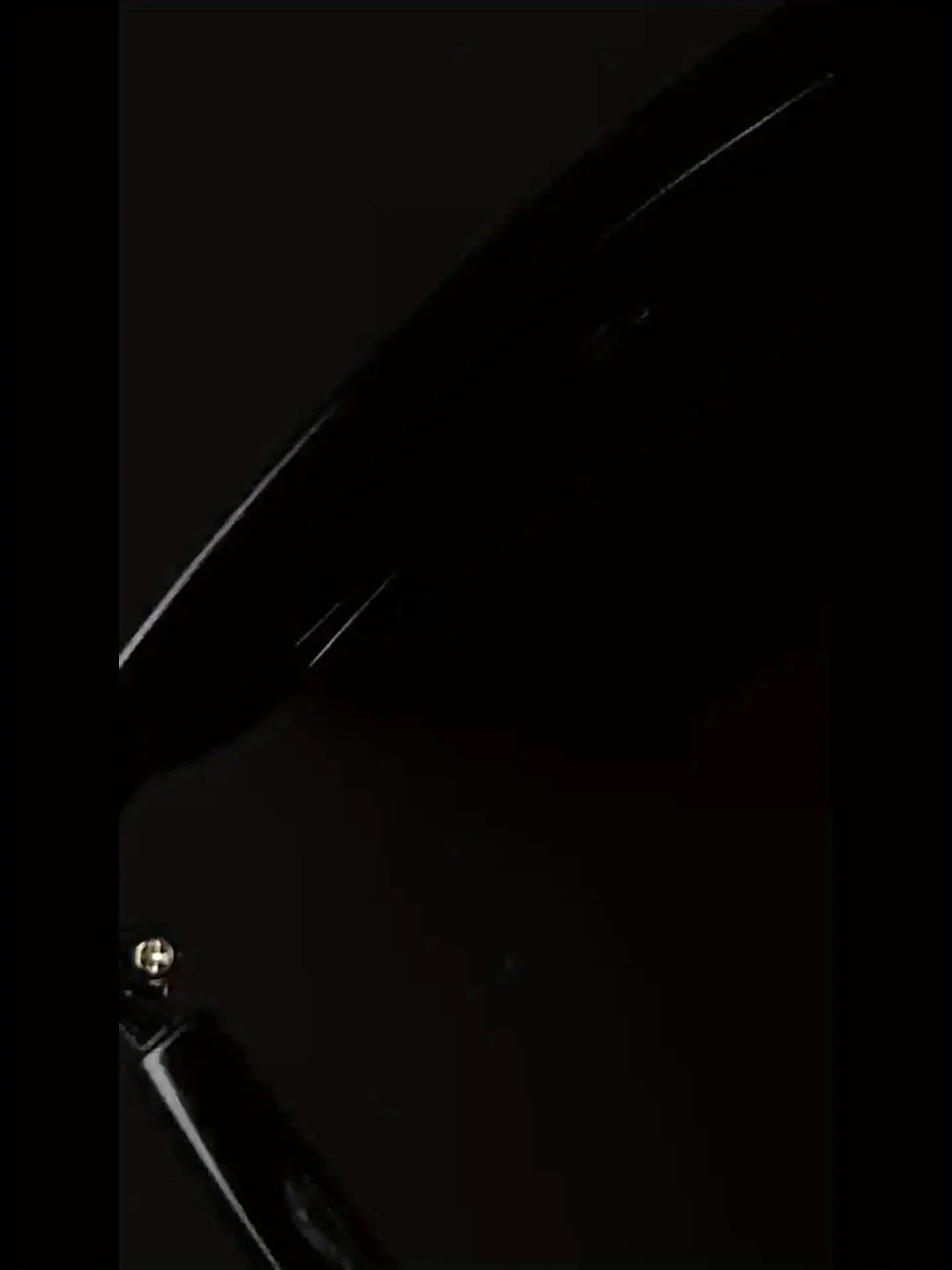 Close-up of glossy black electronic device with visible screw and curved edge on dark background