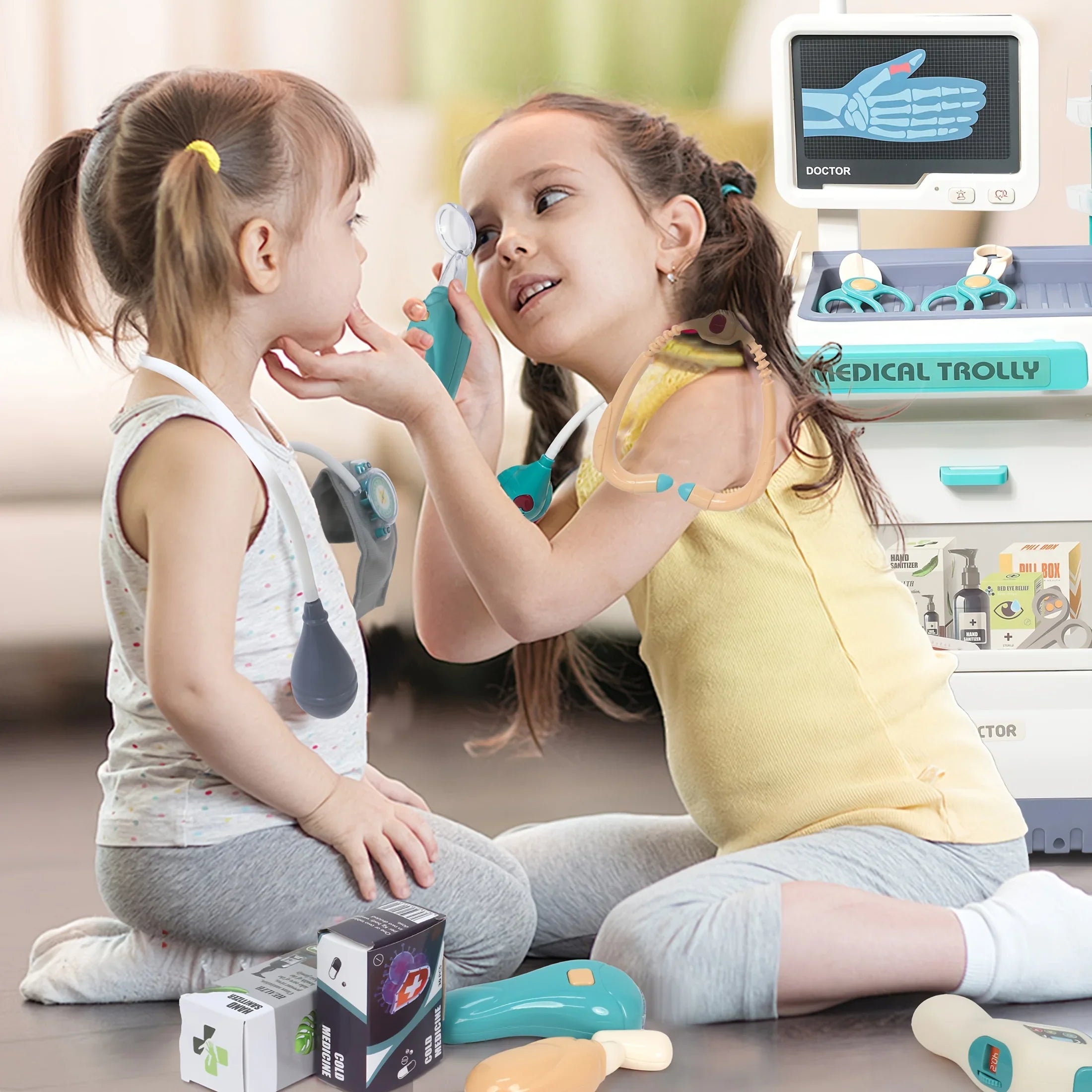 Two young girls playing doctor with STEM medical toys and a toy medical trolley indoors.